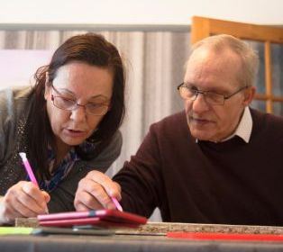 Two people sitting together at a table, reviewing documents and writing notes during a conversation.