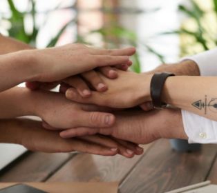 A group of people placing their hands together in a supportive stack on a table, symbolising connection, teamwork and community.