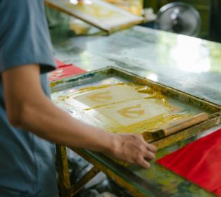 Close-up of a person screen printing, using a mesh frame and ink to transfer a design onto paper in a printmaking workshop setting