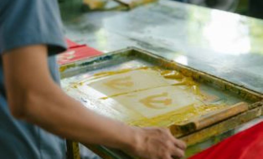 Close-up of a person screen printing, using a mesh frame and ink to transfer a design onto paper in a printmaking workshop setting