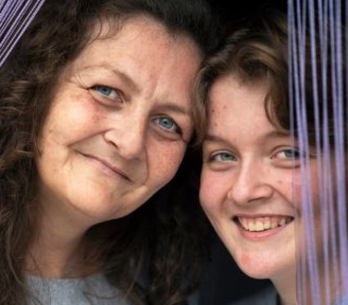 Daisy and her mum smile at the camera framed in a window looking out