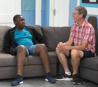  A young carer and adult worker sitting on a sofa in a community room, engaged in conversation.